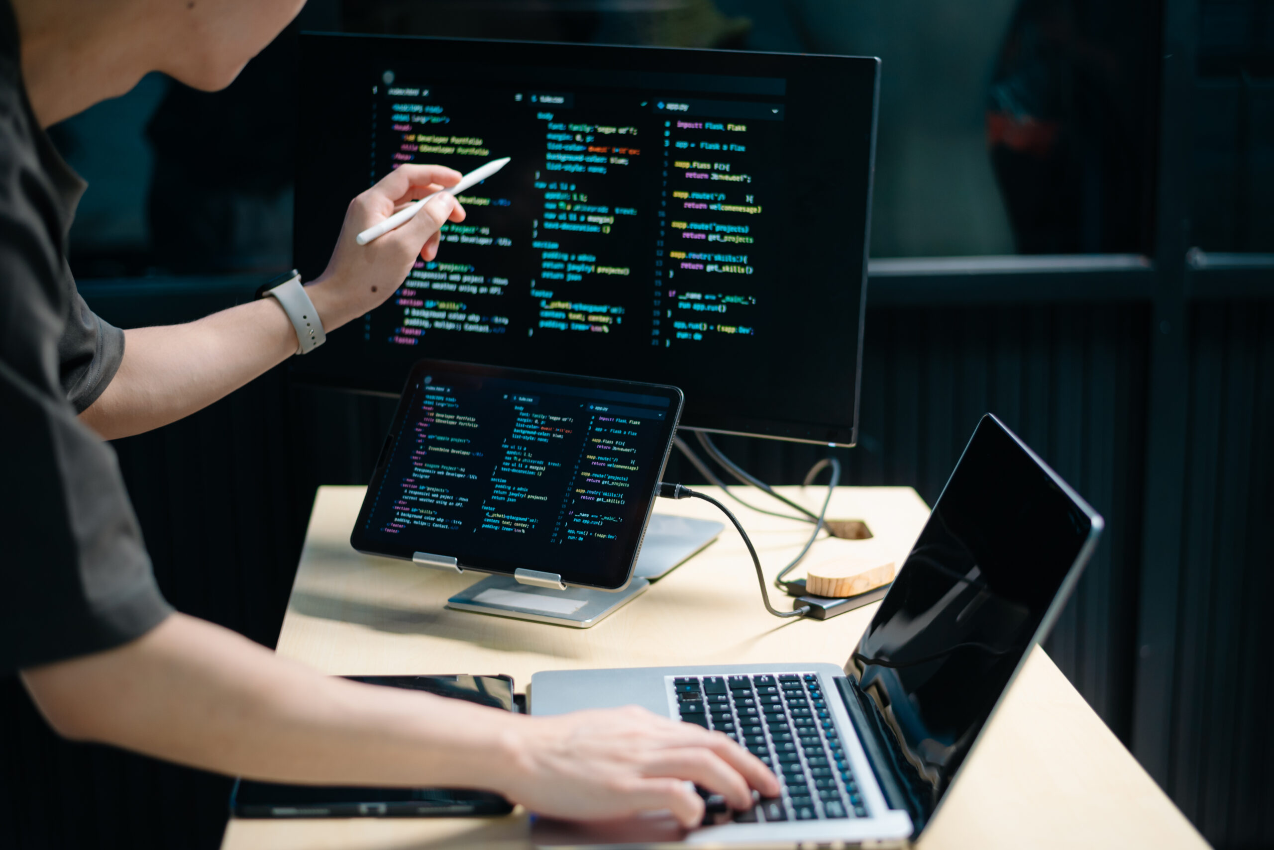 Asian male programmer using stylus to analyze code on tablet and monitor. Software development, coding, and tech workspace concept with real people.